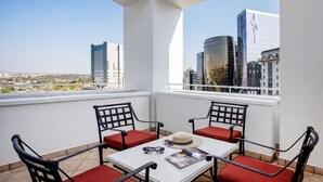 A balcony with a white table, red cushioned chairs, and a view of city buildings. - NH Johannesburg Sandton Hotel (Johannesburg)
