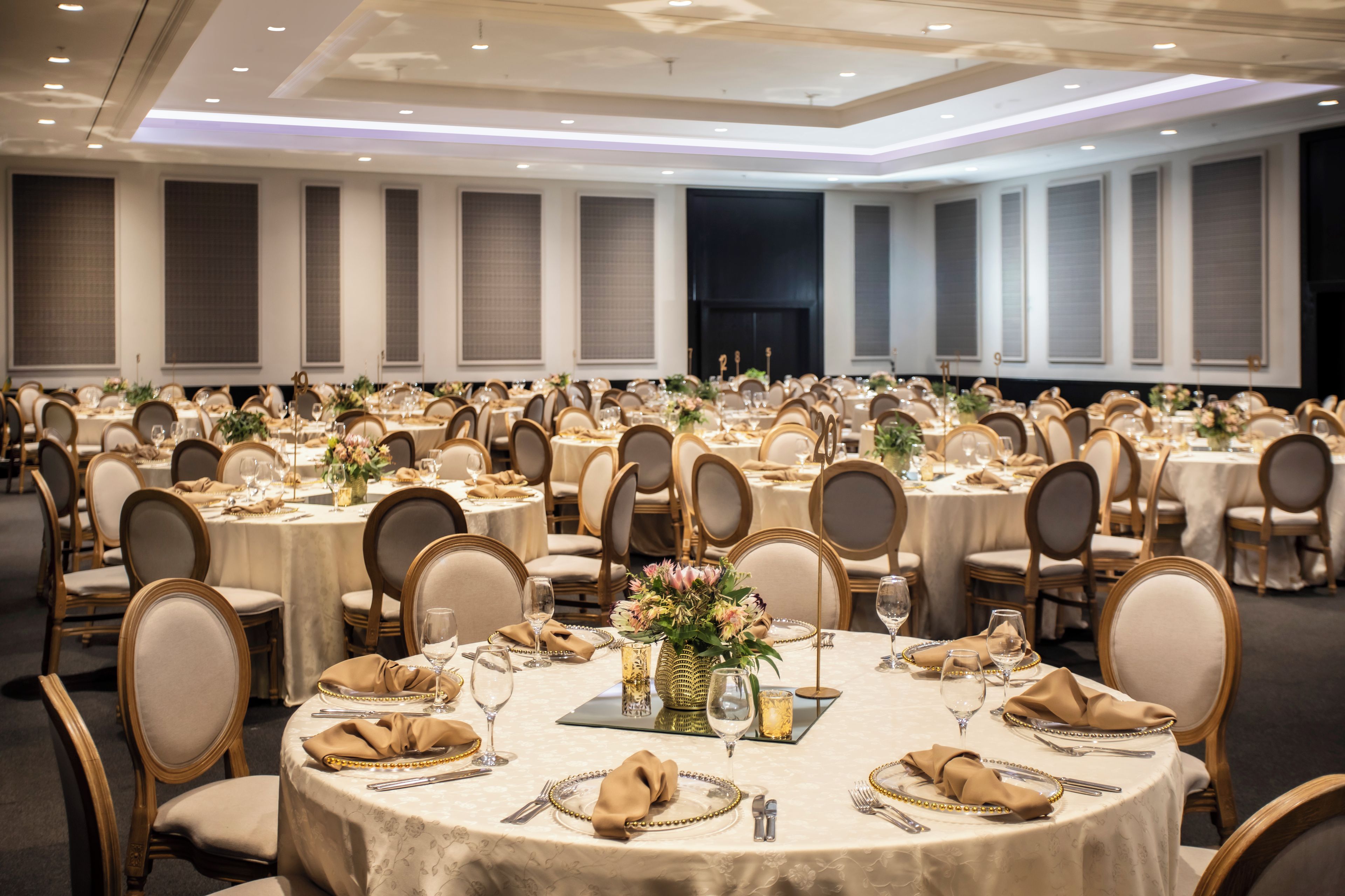 A banquet hall with round tables, each set with place settings, chairs, and floral centerpieces.