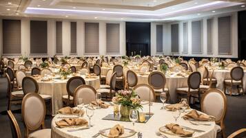 A banquet hall with round tables, each set with place settings, chairs, and floral centerpieces.