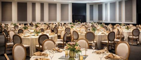 A banquet hall with round tables, each set with place settings, chairs, and floral centerpieces.