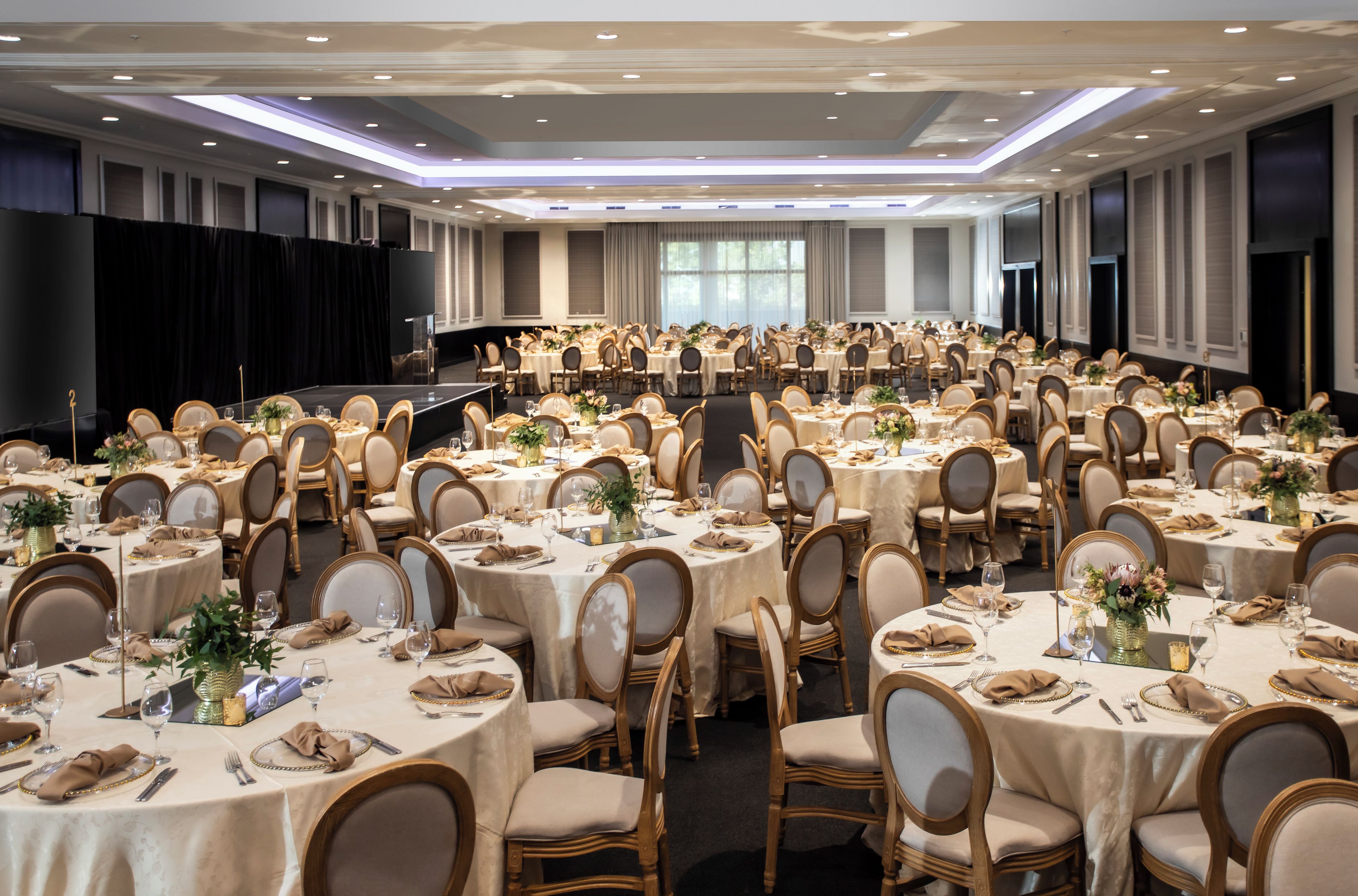 A banquet hall with round tables, chairs, and a stage.