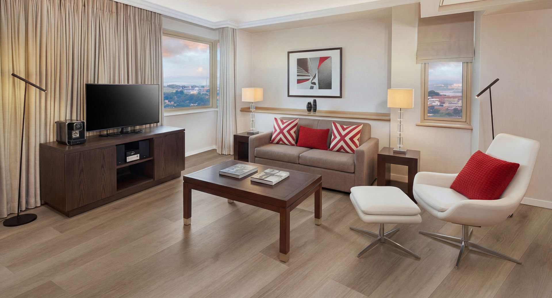 Una habitación de hotel moderna con una televisión de pantalla plana, un sofá, un sillón blanco, una mesa de centro y vistas a la ciudad.