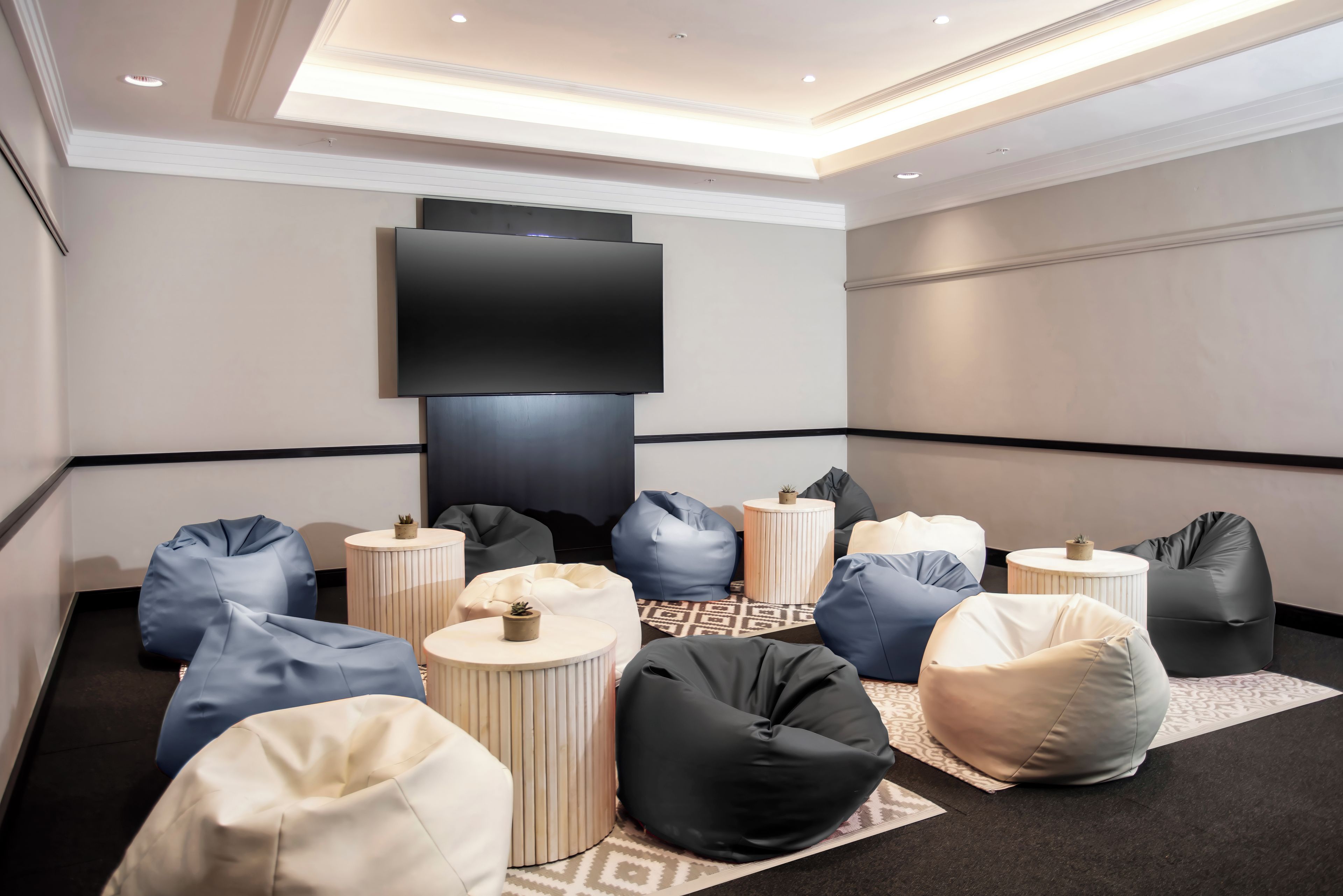 A modern lounge area with a flat-screen TV mounted on the wall, surrounded by multiple bean bags and small round tables.