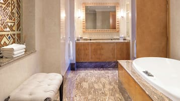 A modern bathroom with a large bathtub, a double sink vanity, a bench, and a decorative wall tile.