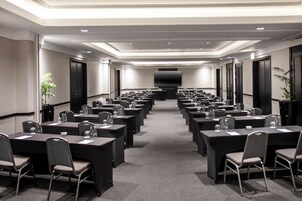 A conference room with rows of tables and chairs, a large screen at the front, and a modern ceiling design.