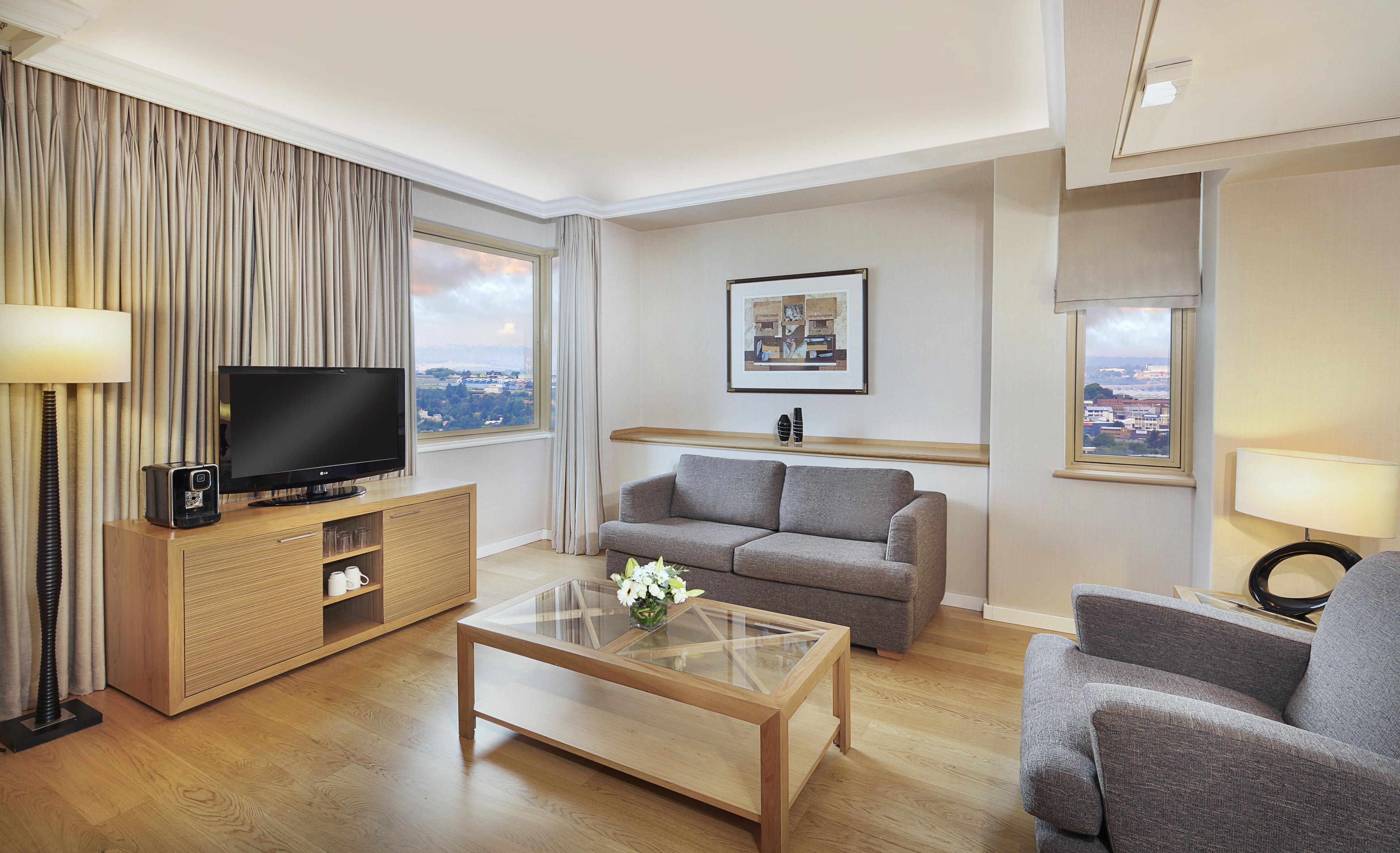A modern living room with a flat-screen TV, a sofa, a coffee table, and a view of the city through large windows.