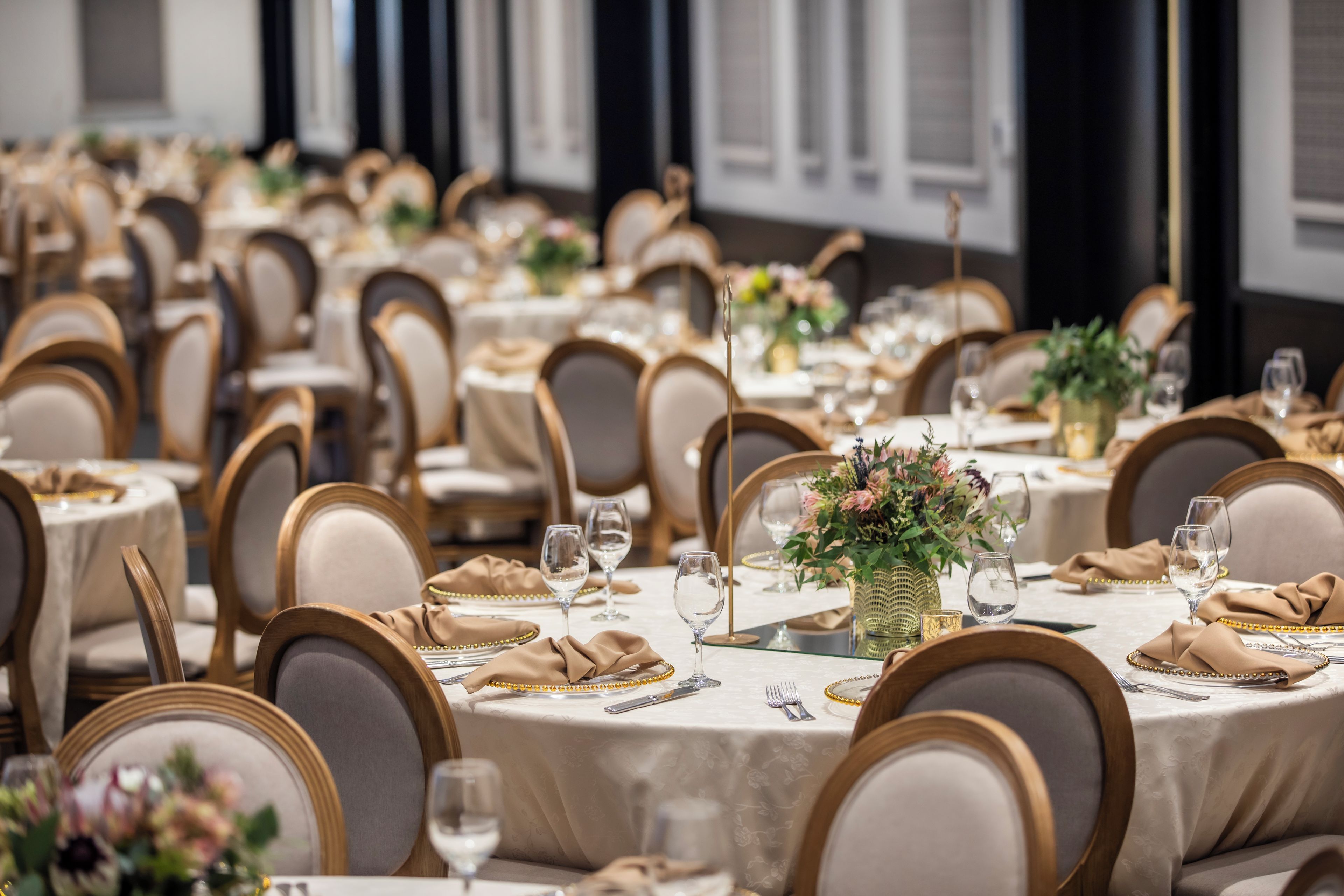 Een feestzaal met ronde tafels gedekt voor een diner, met gouden accenten en bloemstukken.