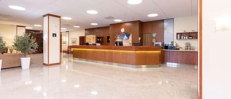 Zona de recepción de un hotel con un mostrador de madera, un reloj y una máquina de café.