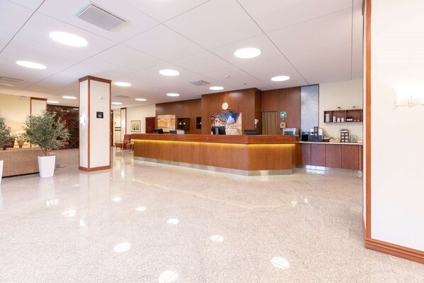 A hotel reception area with a wooden reception desk, a clock, and a coffee machine.