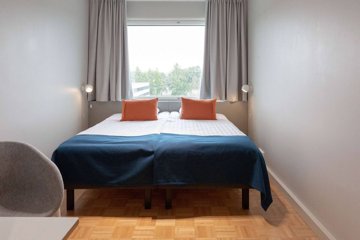 A bedroom with a bed, two pillows, a chair, and a window with curtains.
