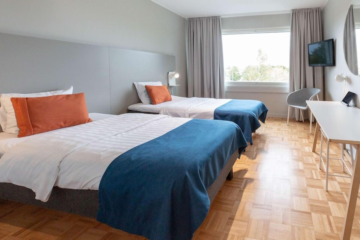 Habitación de hotel con dos camas, un escritorio, una silla, un televisor y una ventana con cortinas.
