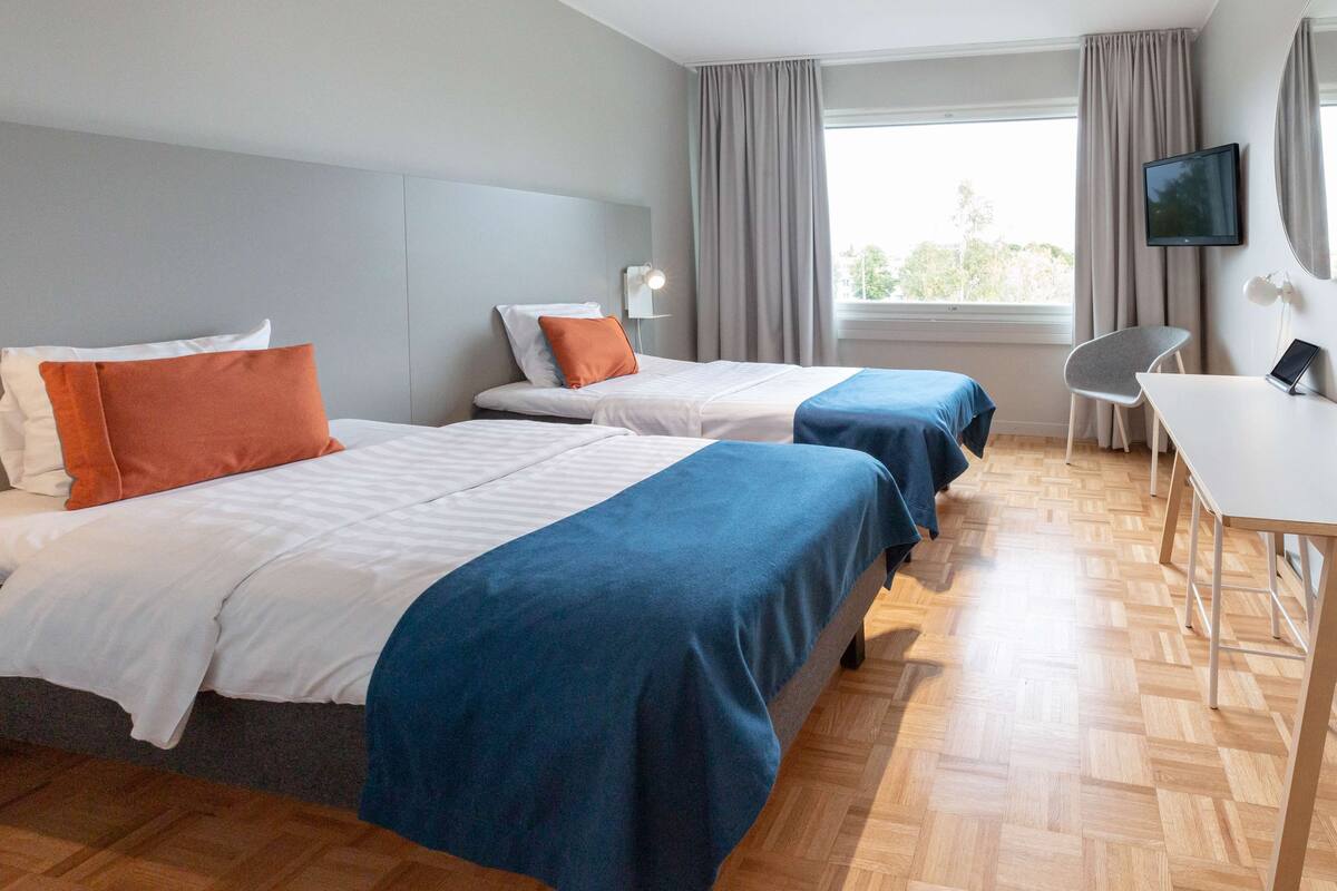 A hotel room with two beds, a desk, a chair, a TV, and a window with curtains.