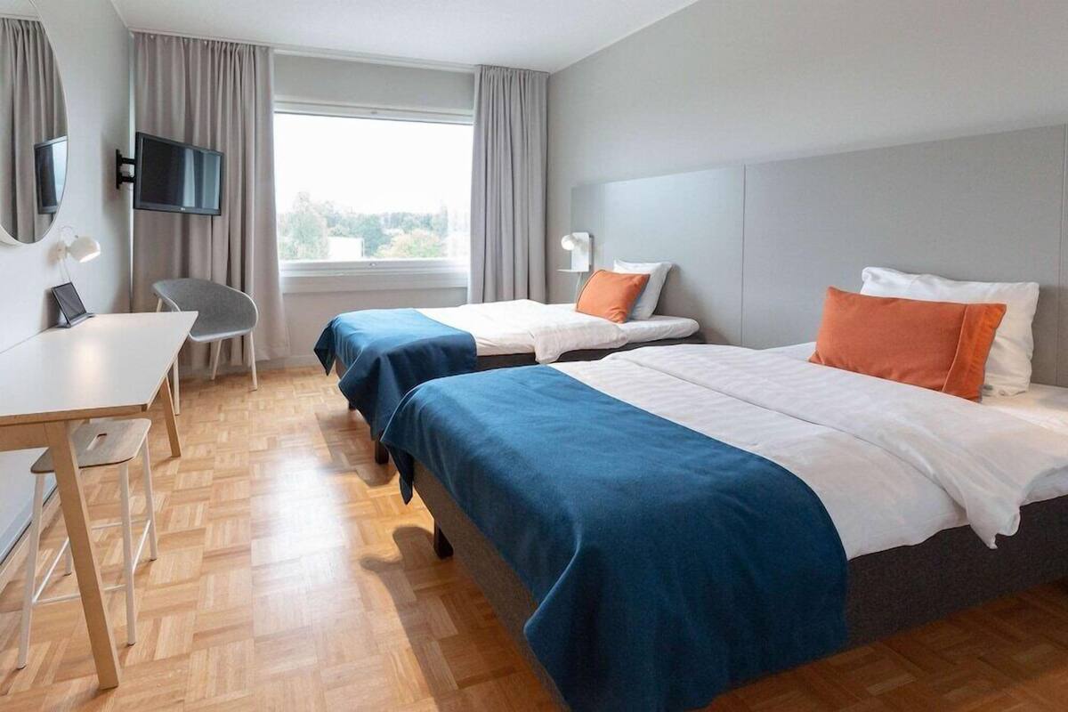 A hotel room with two beds, a desk, a chair, a TV, and a window with curtains.