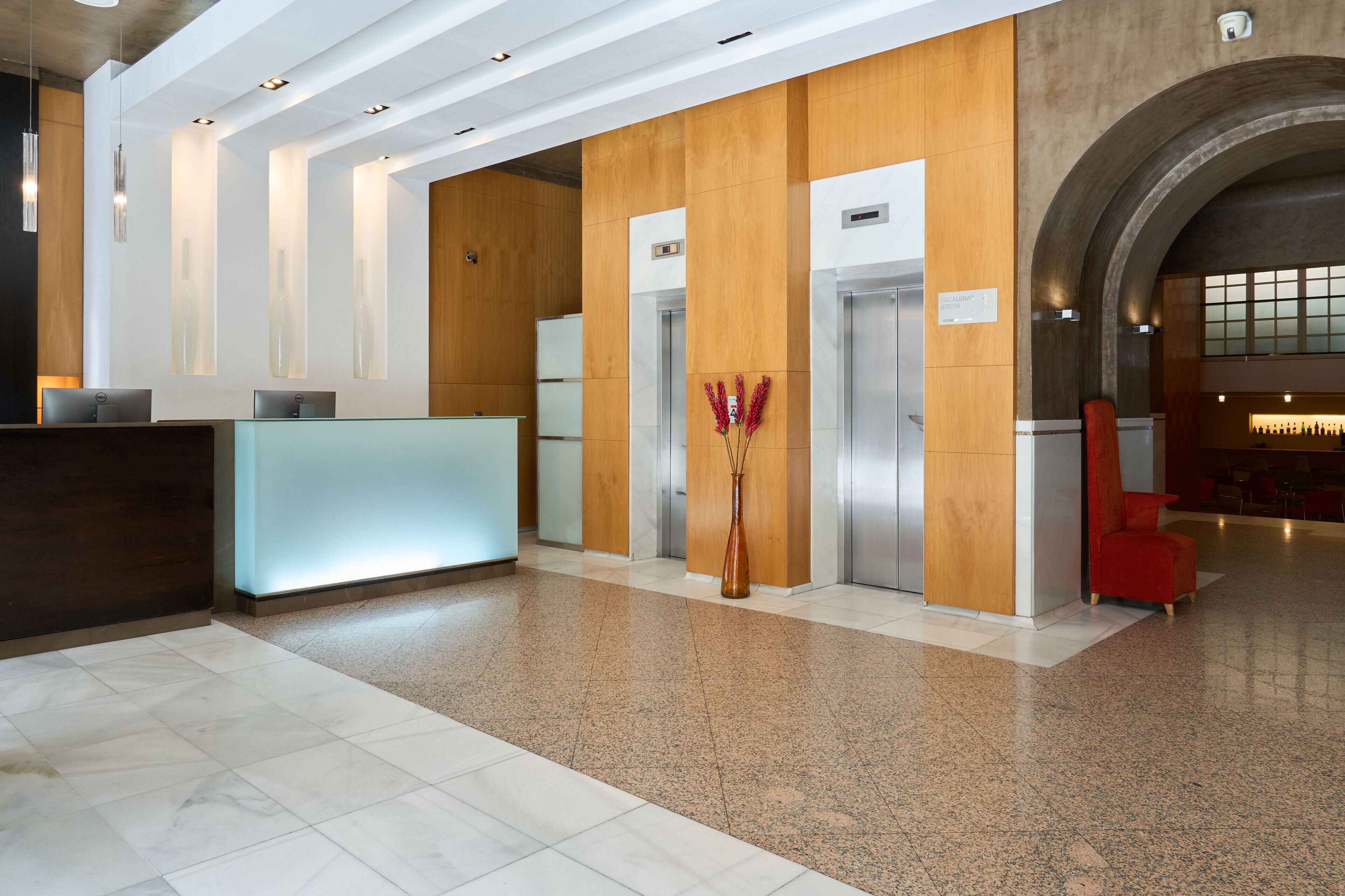 Um hall moderno com balcão de recepção, elevadores e uma cadeira vermelha.