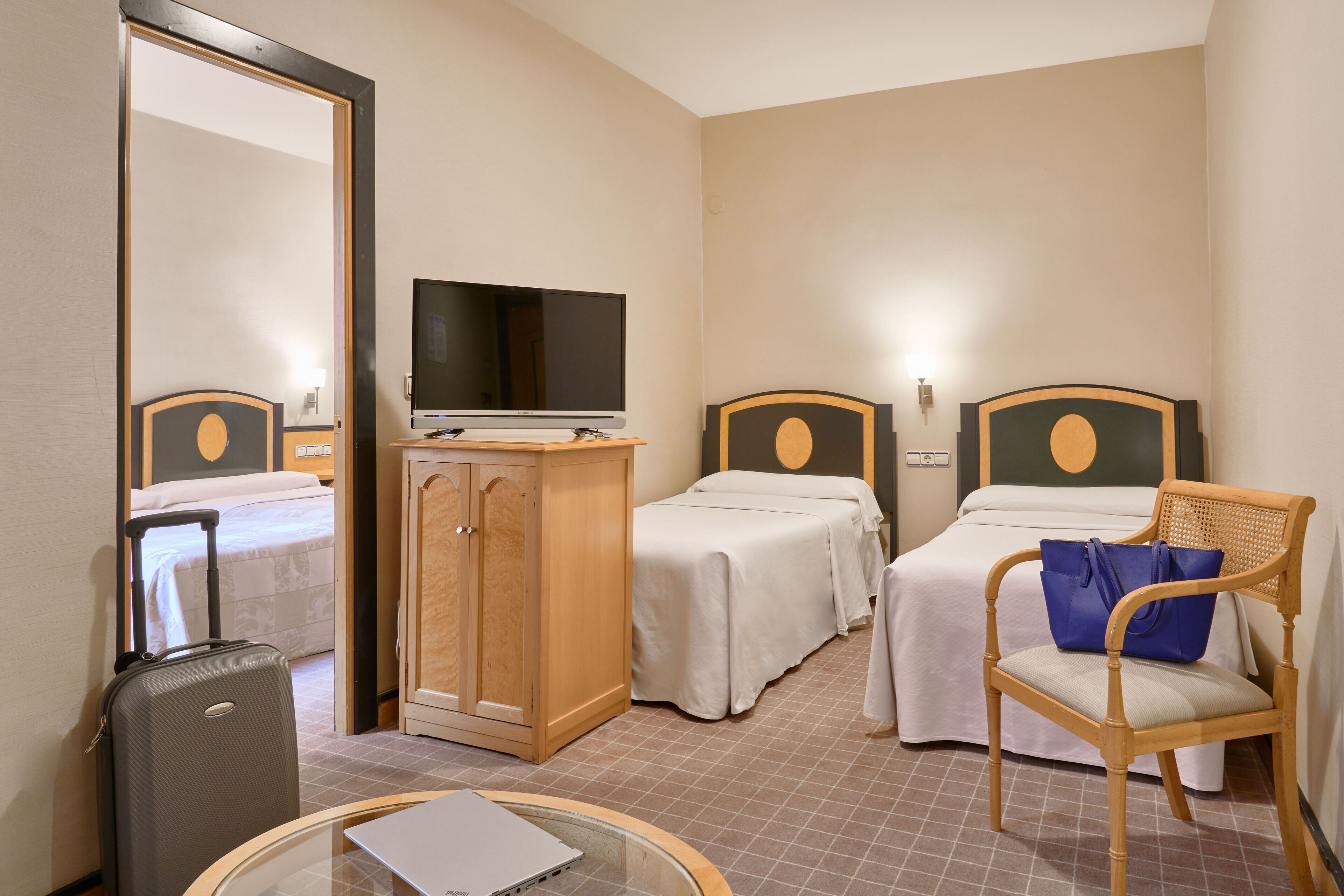 Ein Hotelzimmer mit einem Bett, einem Schreibtisch, einem Sessel, einem Fernseher und einem Koffer.