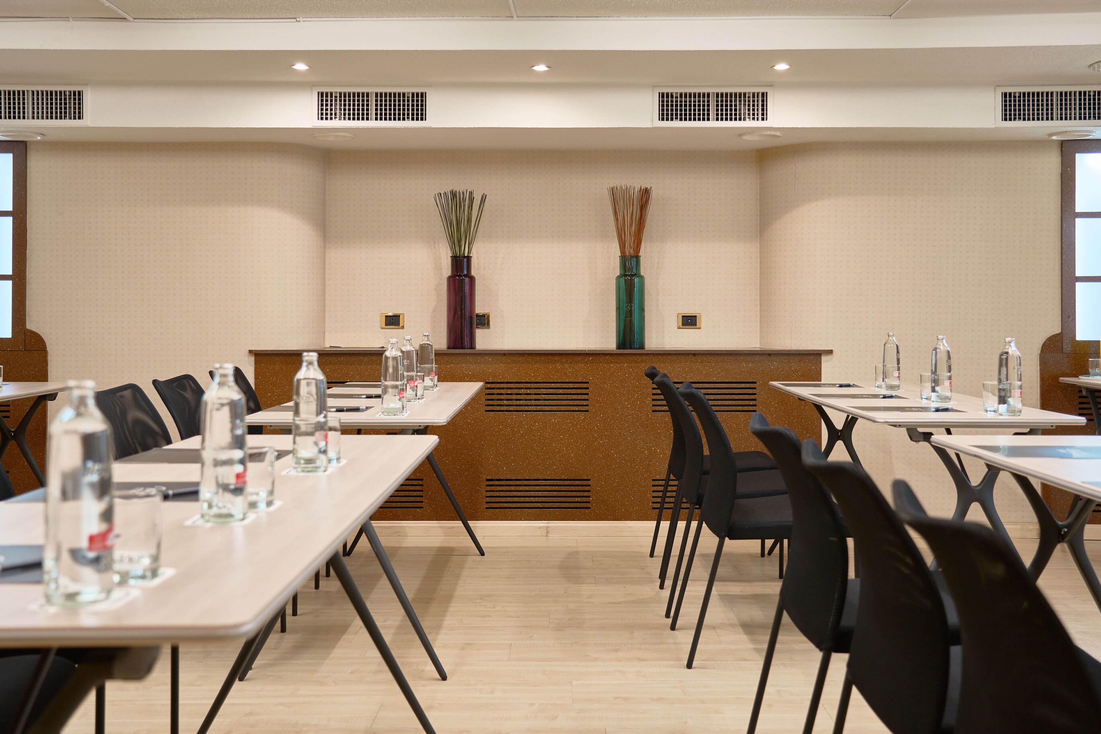A conference room with tables, chairs, water bottles, and two decorative vases on the wall.