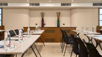 A conference room with tables, chairs, water bottles, and two decorative vases on the wall.