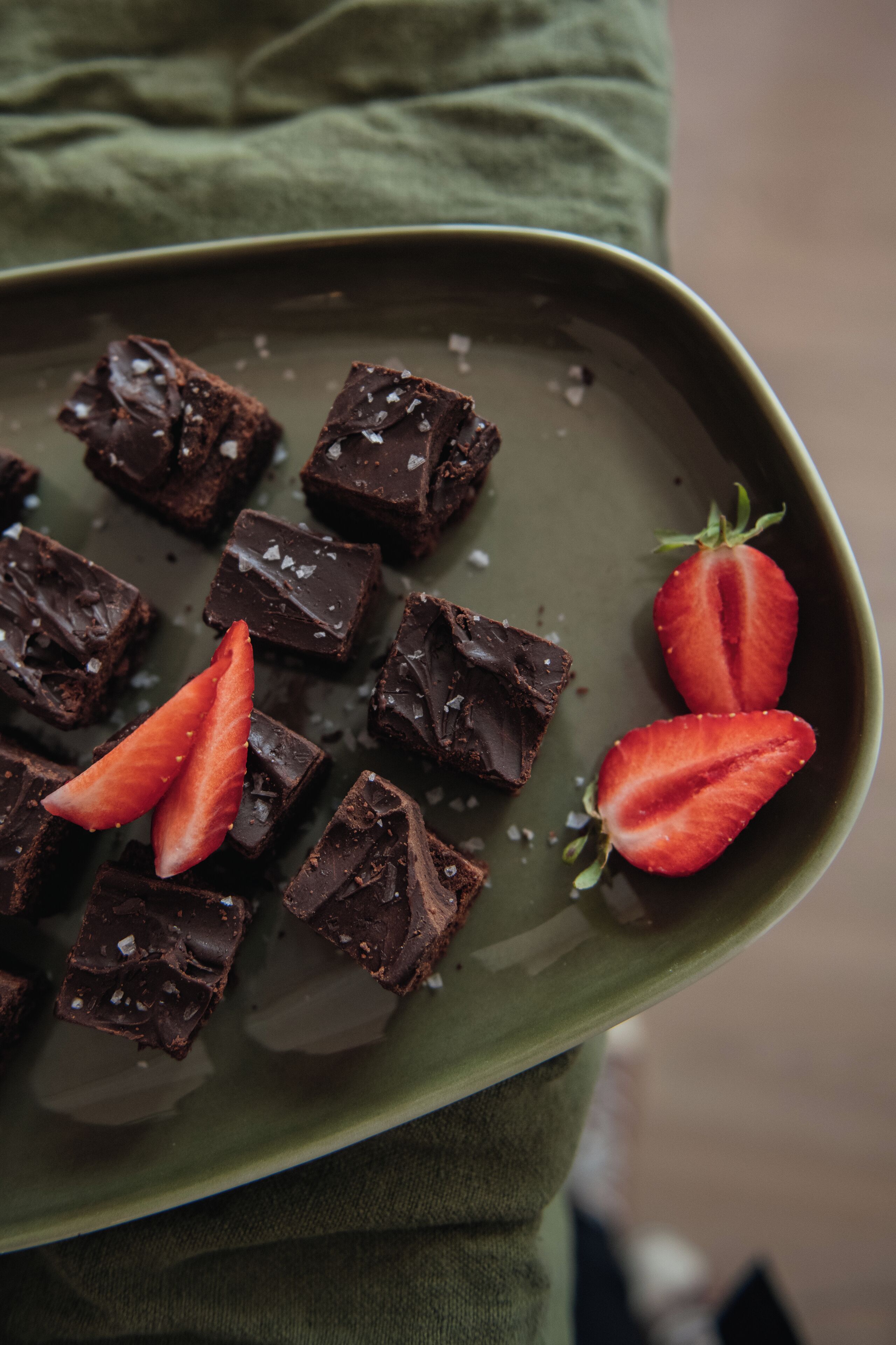 A green plate with chocolate squares and strawberries.