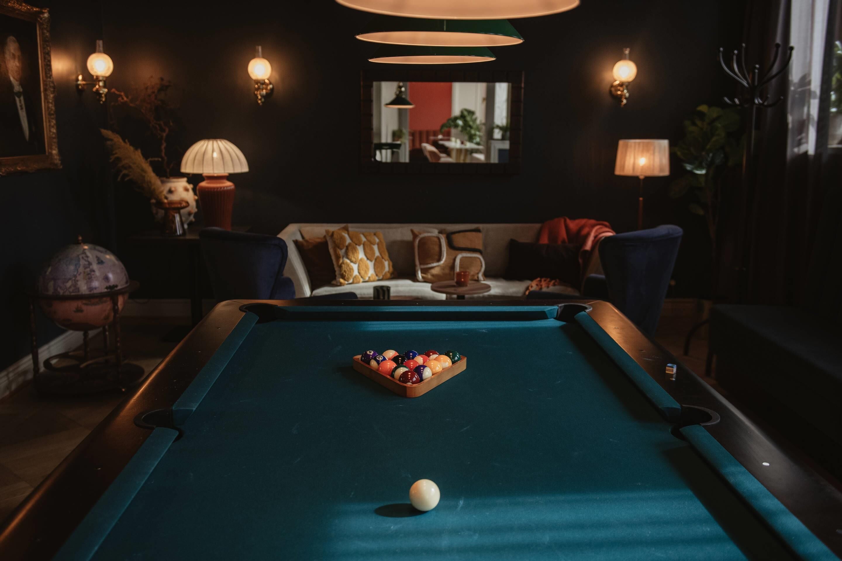 Una mesa de billar con bolas, un sofá y apliques en una habitación con poca luz.