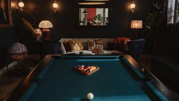 Una mesa de billar con bolas, un sofá y apliques en una habitación con poca luz.