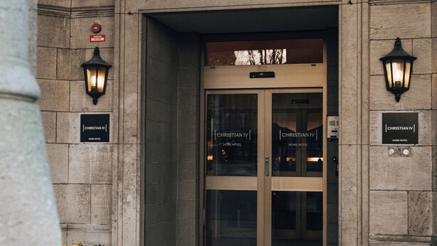A hotel entrance with double doors, a sign above the doors, and two wall-mounted light fixtures. - Home Hotel Christian IV (Kristianstad)