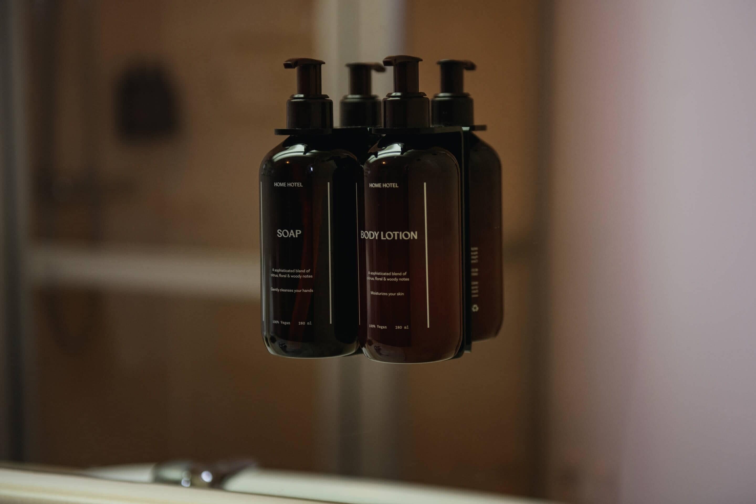 Three bottles of soap and lotion labeled 'HOME HOTEL' on a shelf.