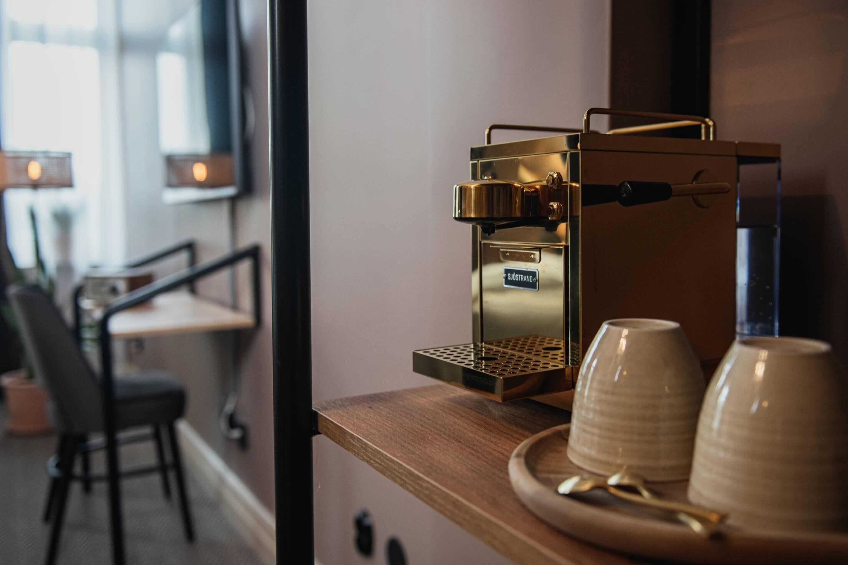 A coffee machine on a wooden counter with two ceramic cups and a spoon.