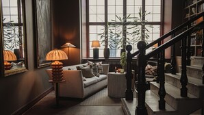 A cozy living room with a sofa, a side table with a lamp, and a staircase. - Home Hotel Christian IV (Kristianstad)