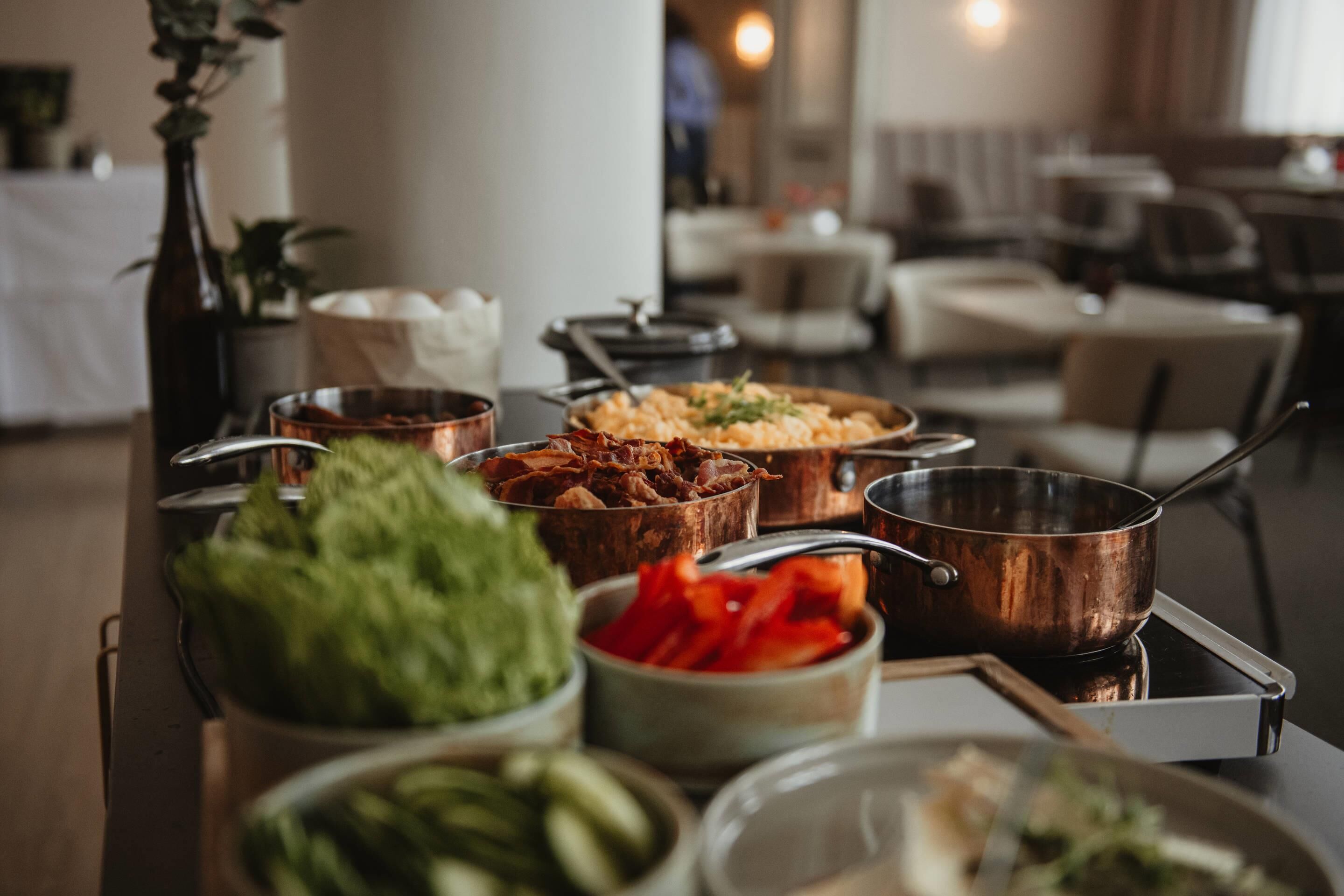 A buffet table with various dishes and a copper pot on a tray.