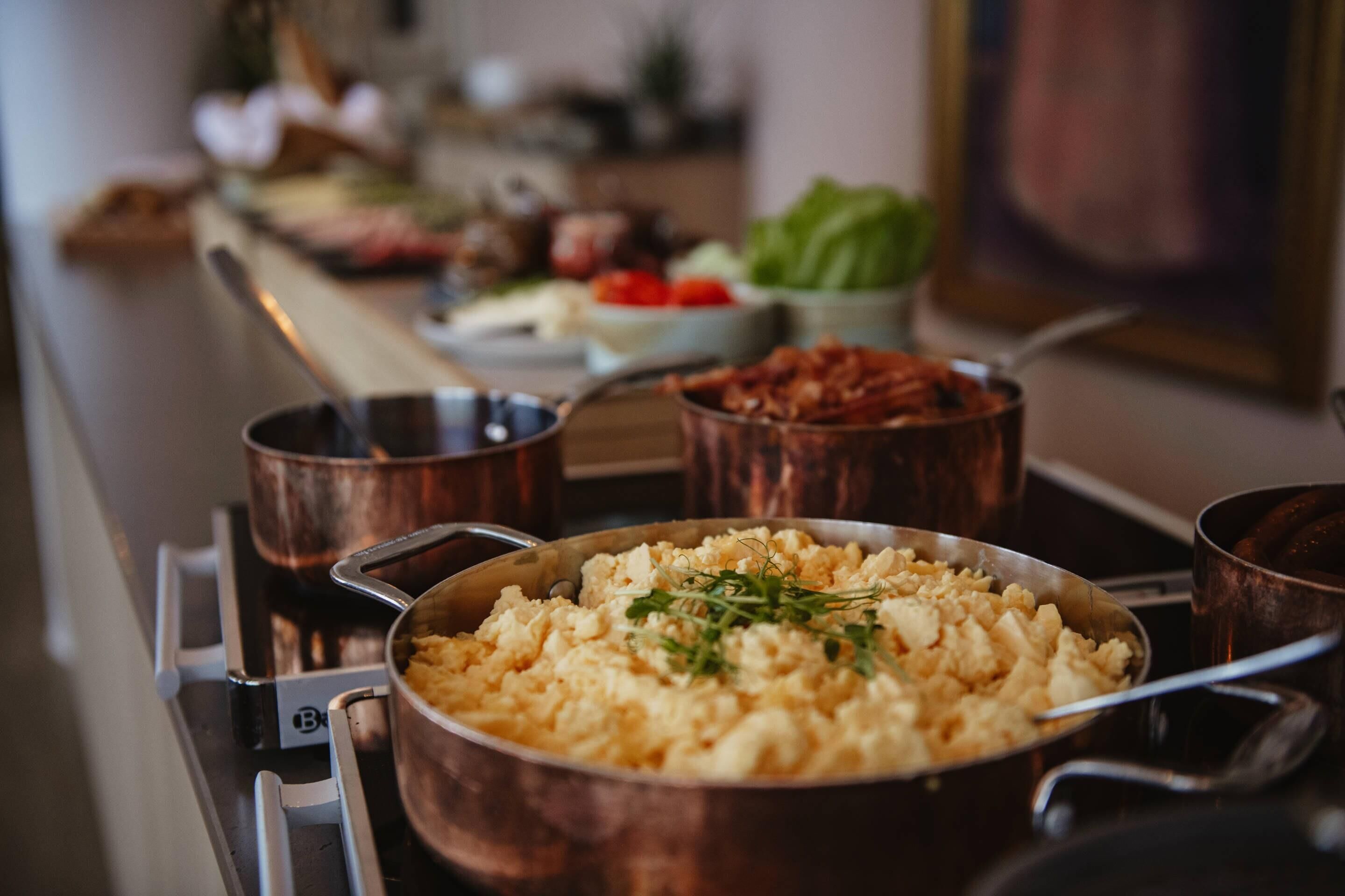 A kitchen counter with various cooking pots and pans, including a large pan of scrambled eggs garnished with herbs.