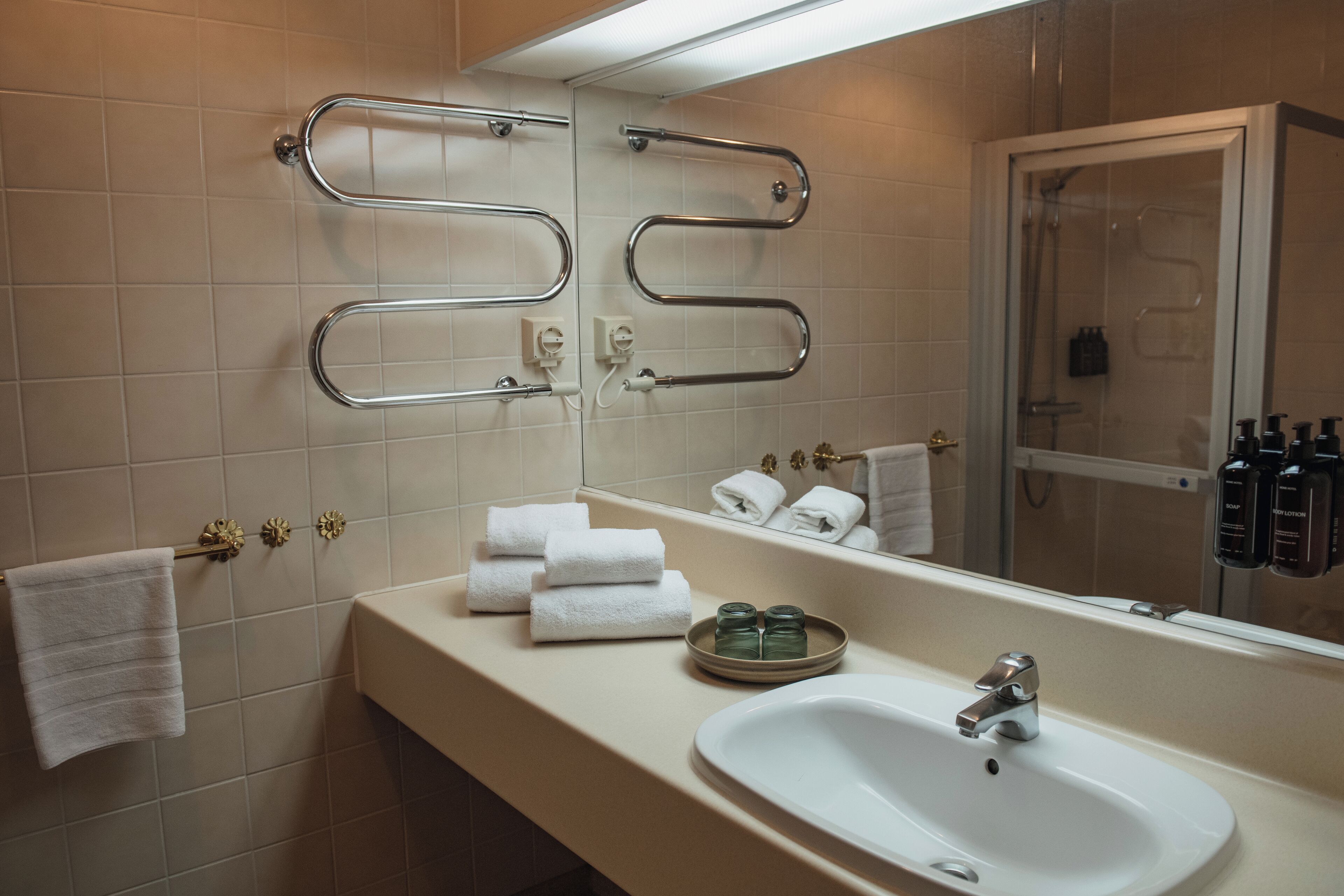 Ein Badezimmer mit Waschbecken, Spiegel, Handtuchhalter und Duschbereich.