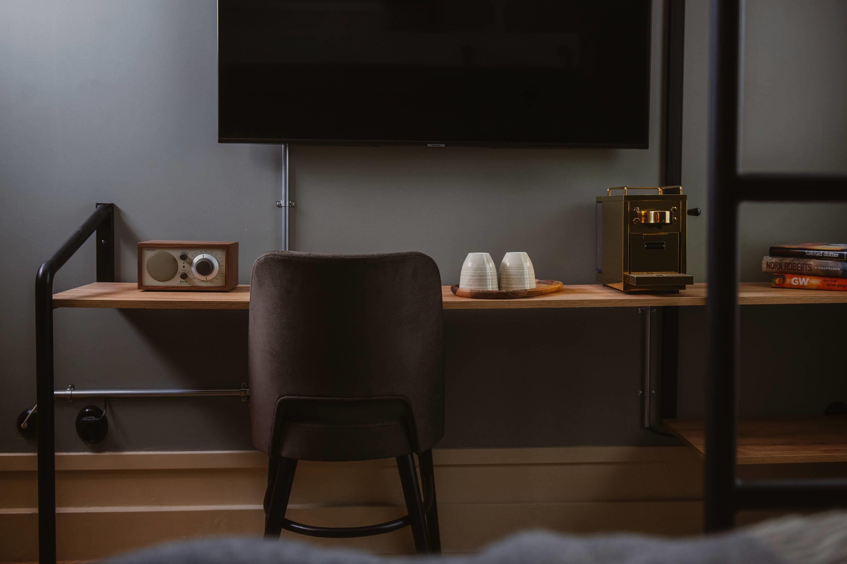 Een moderne kamer met een flatscreen televisie aan de muur, een houten bureau met een vintage radio, twee kopjes en een kluis.