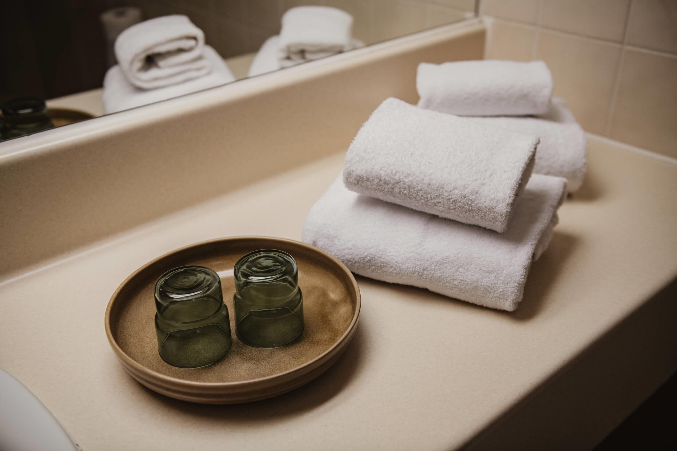 Une salle de bain avec une baignoire, deux bouteilles en verre posées sur une assiette et plusieurs serviettes blanches pliées.