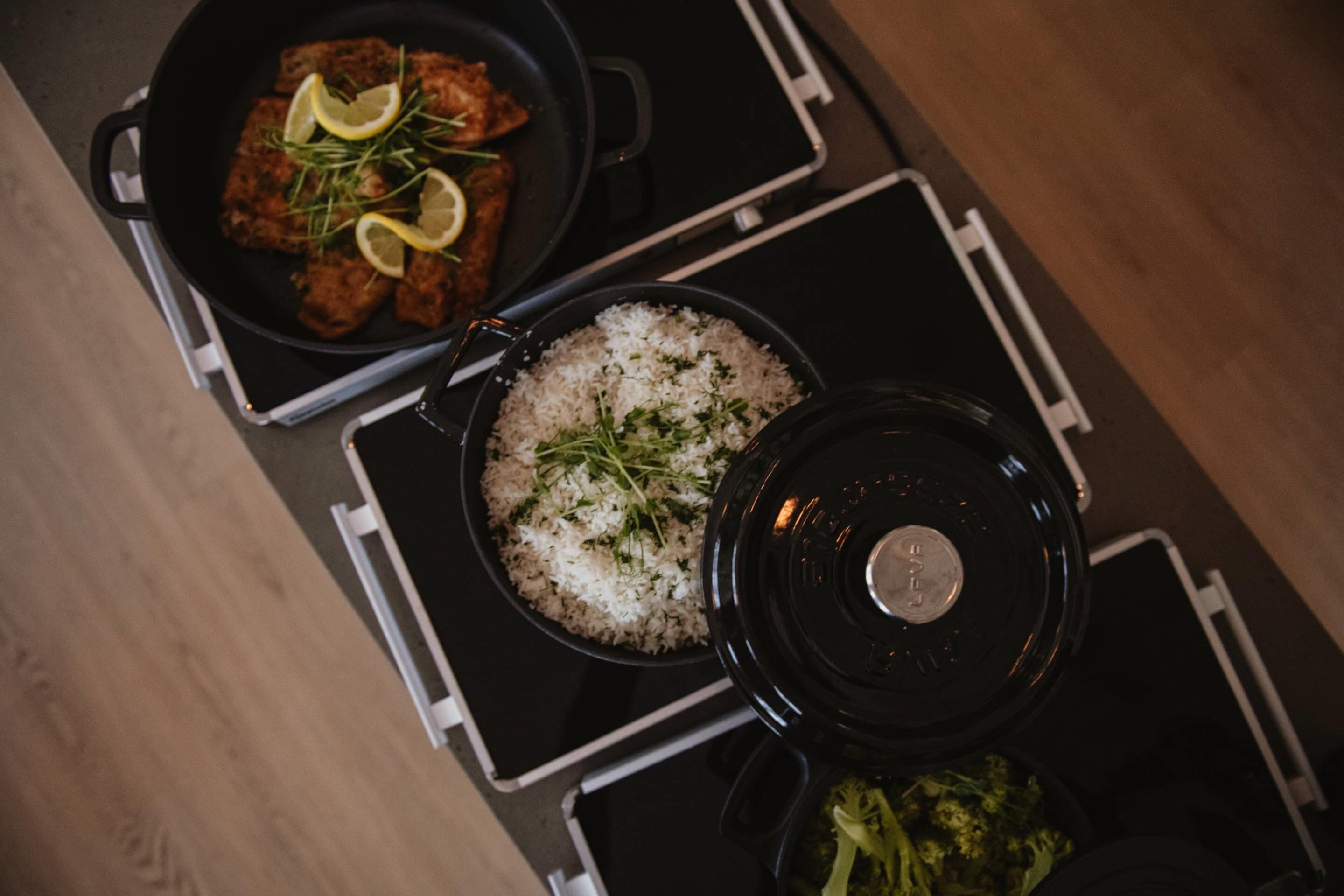 A kitchen with a stove, a pan with food, a pot of rice, and a lid.