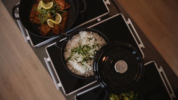 A kitchen with a stove, a pan with food, a pot of rice, and a lid.