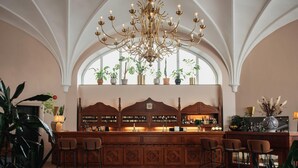 A bar area with a wooden counter, multiple chairs, a chandelier, and potted plants. - Home Hotel Christian IV (Kristianstad)