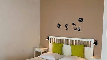 Un dormitorio con una cama blanca, almohadas verdes y blancas, una mesita de noche blanca, una lámpara de pared y un candelabro.