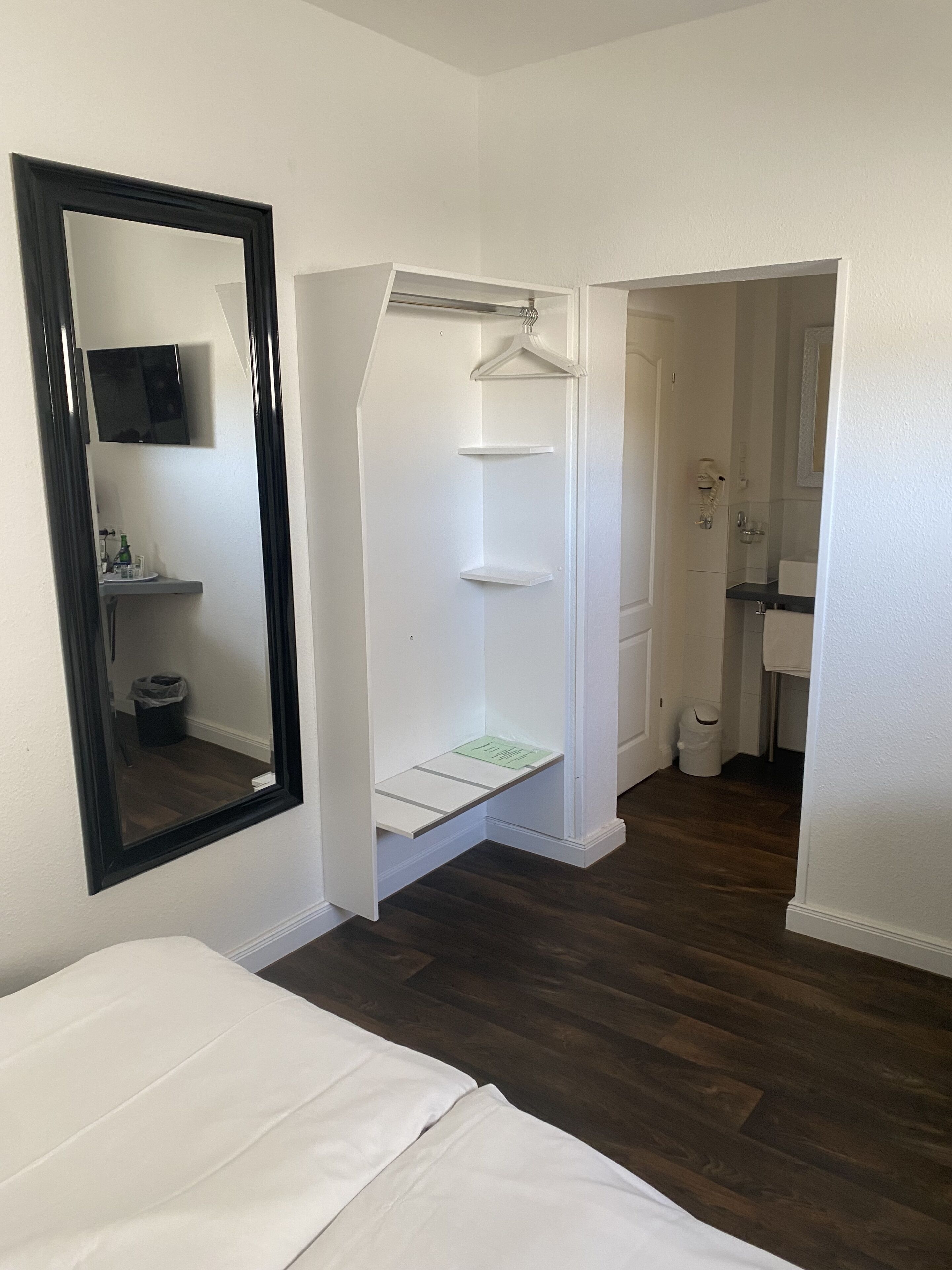 A bedroom with a bed, a mirror, a walk-in closet with shelves, and a bathroom with a sink and toilet.