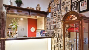 Zona de recepción de un hotel con un mostrador de madera, un reloj y una pared decorada con fotografías enmarcadas.