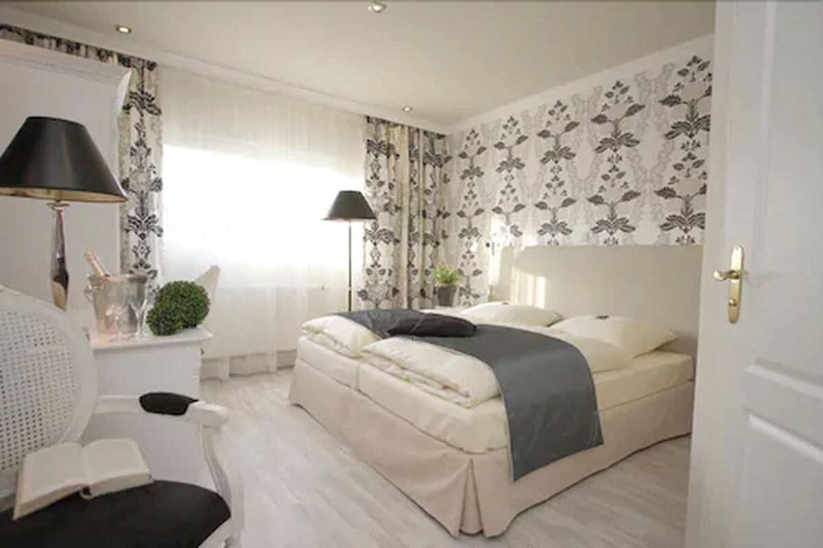 A bedroom with a bed, bedside lamps, a desk with a chair, and a window with curtains.