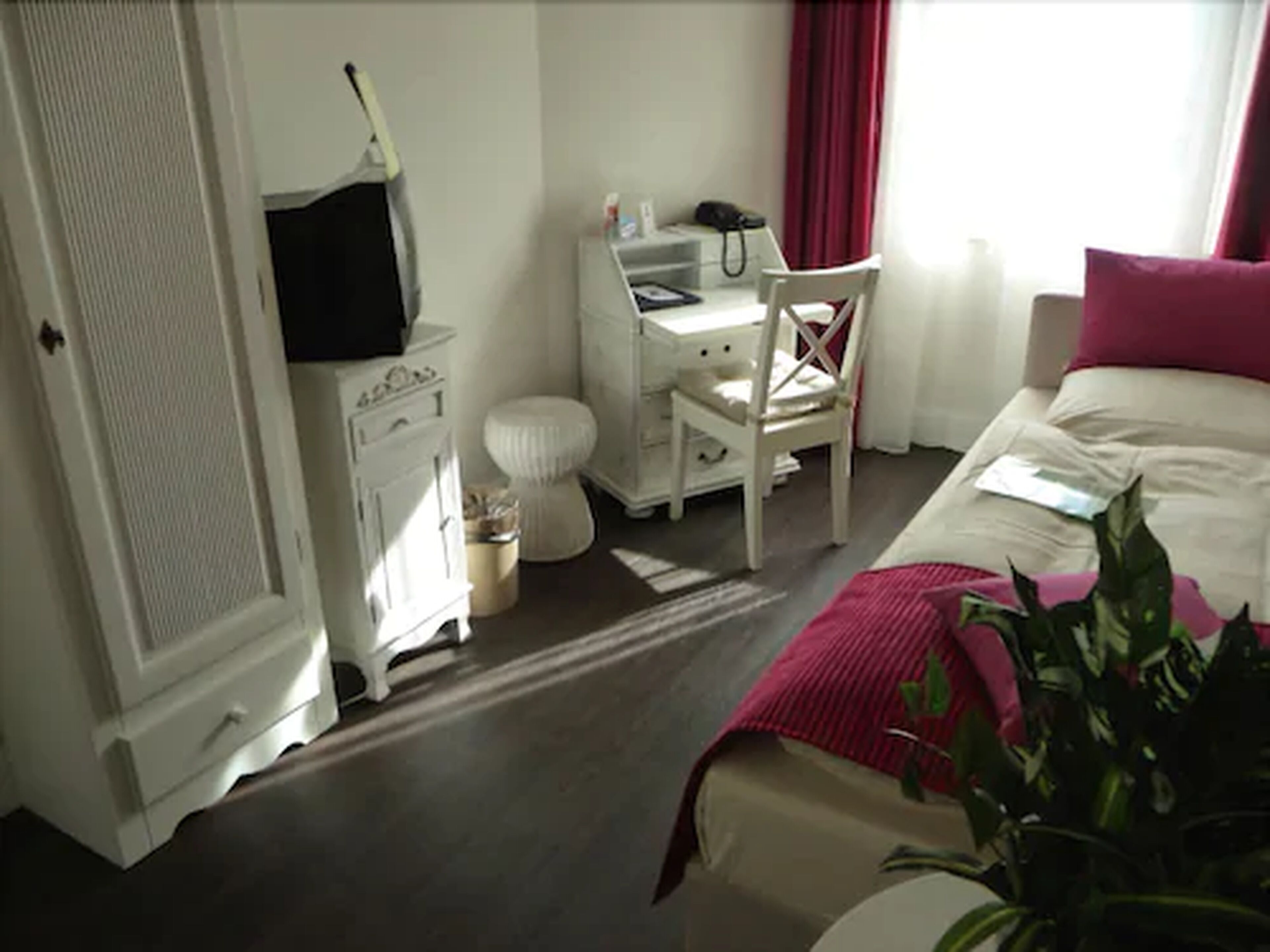Une chambre d’hôtel comprenant un lit, un bureau, une chaise, une petite table, une poubelle et une plante en pot.