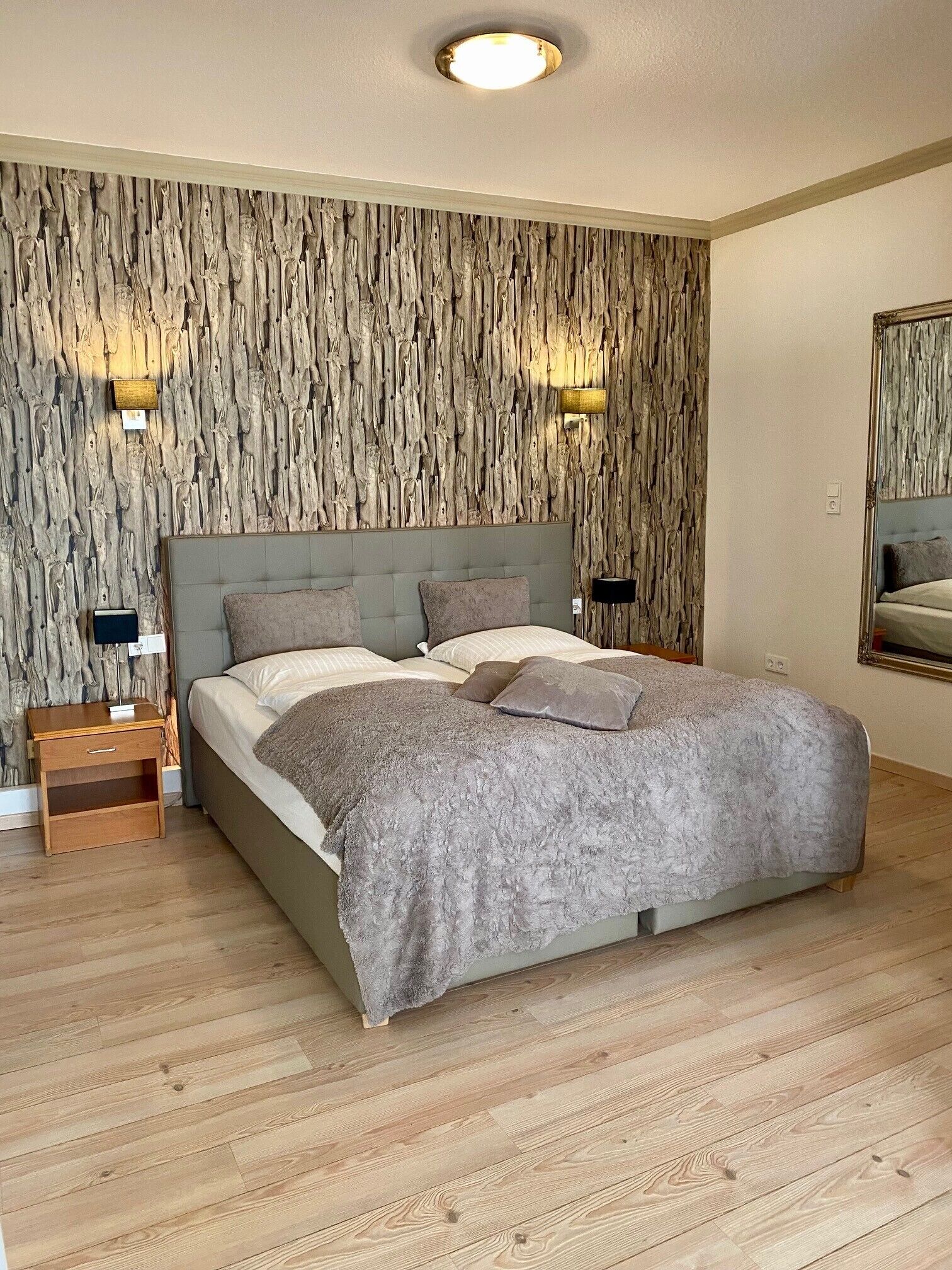 Ein Schlafzimmer mit Holzpaneelen, einem Bett mit grauer Bettwäsche, zwei Nachttischen und einem Beistelltisch.