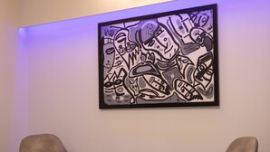 Ein Zimmer mit zwei modernen Stühlen, einem kleinen Tisch und einem Wandbild.