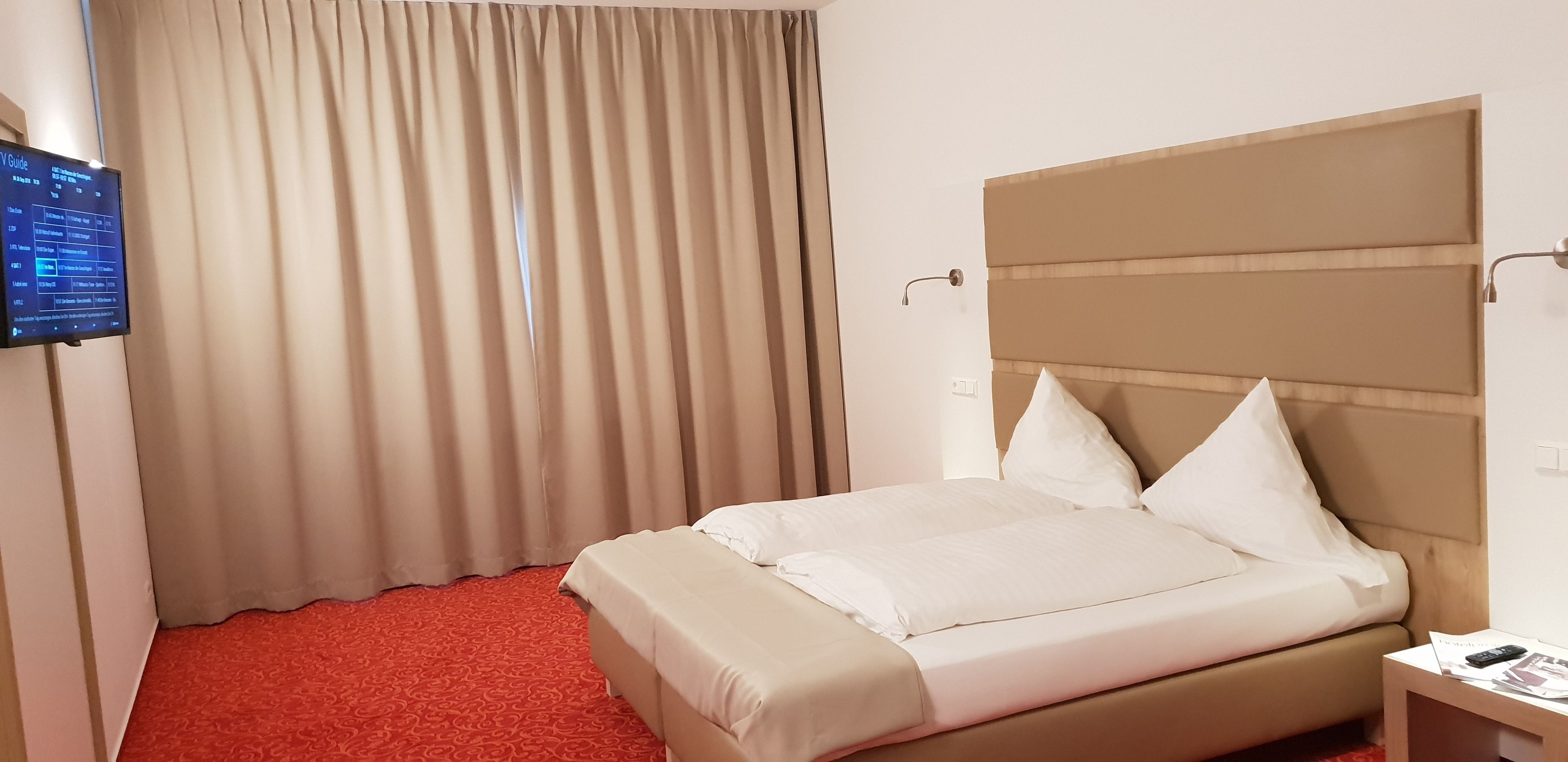 Ein Hotelzimmer mit einem Bett, Vorhängen, einem Fernseher und einem Nachttisch.