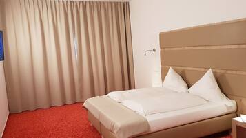 Ein Hotelzimmer mit einem Bett, Vorhängen, einem Fernseher und einem Nachttisch.