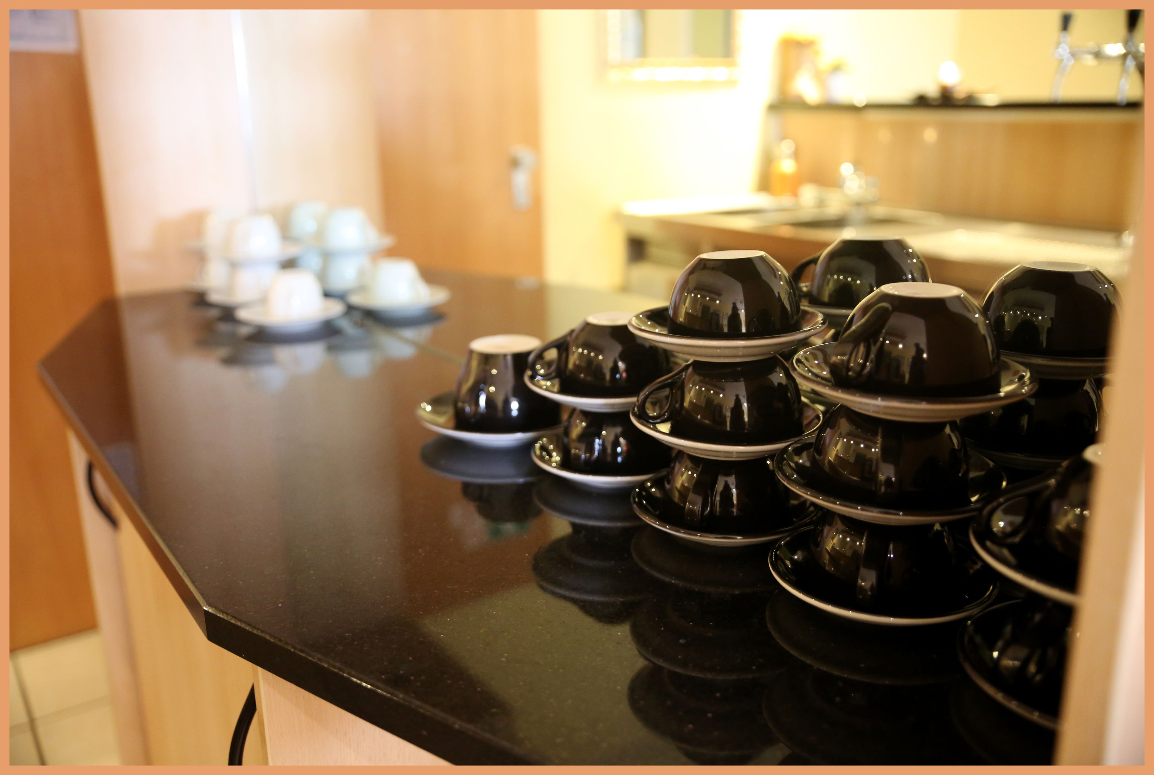 A kitchen counter with multiple black teapots and cups arranged neatly.