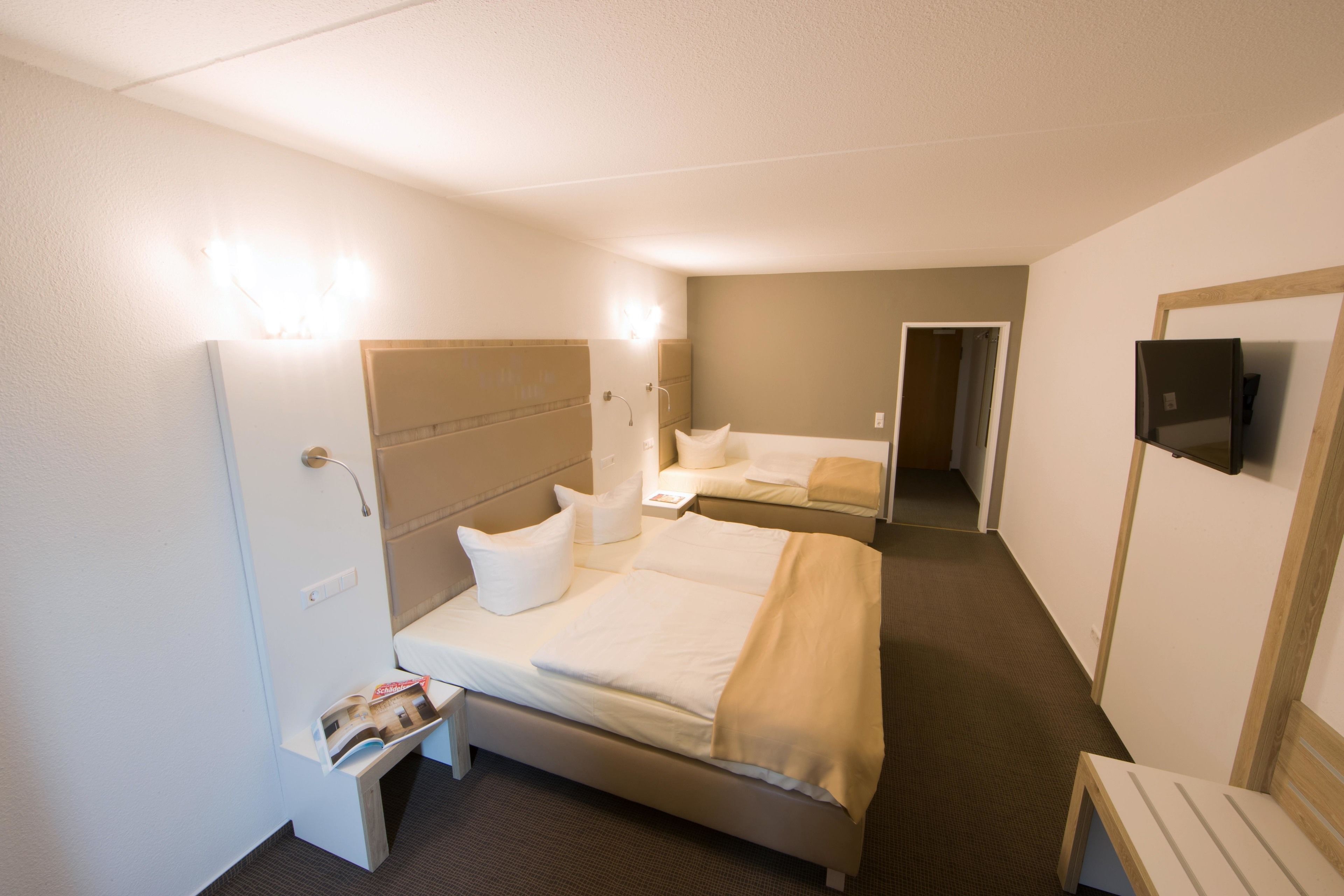 A hotel room with two beds, a TV, a bedside table, and a small seating area.