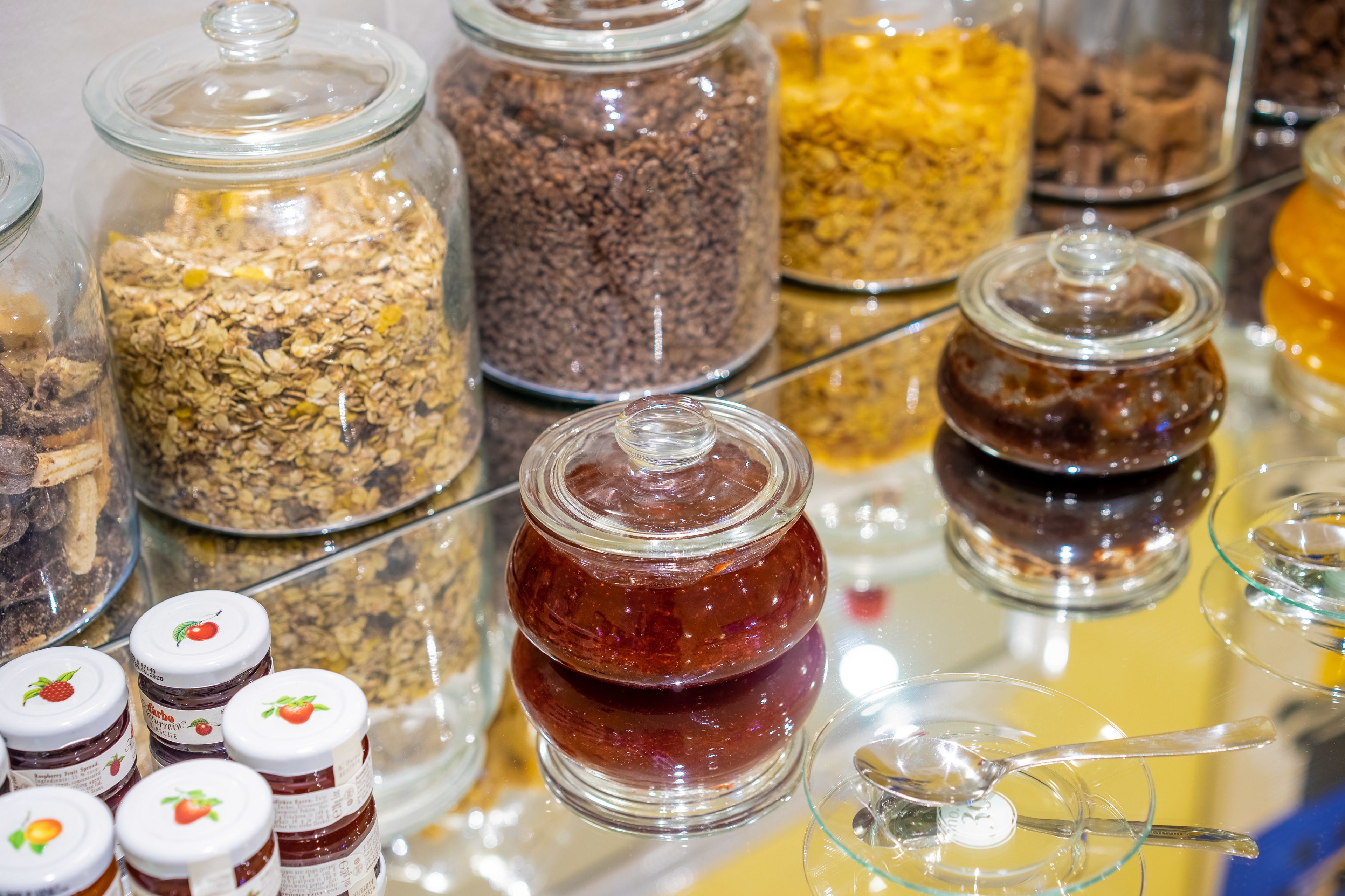 Variedad de alimentos en recipientes de vidrio, como tarros de granola, crema de chocolate y otros bocadillos.