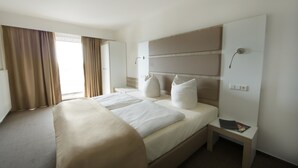 Ein Hotelzimmer mit einem großen Bett, einem Nachttisch mit einer Zeitschrift, einer Ablagefläche und einer Wandlampe.