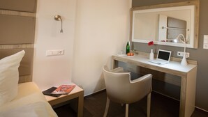 Ein Hotelzimmer mit Bett, Schreibtisch mit Laptop, Stuhl, Spiegel und Dusche.